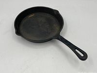 Photo of the full iron fry pan showing overall wear, round shape, long handle, and pouring spouts.