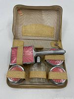 Top view of the beige zipped makeup carrying case open showing five glass containers inside secured with beige straps.