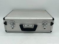 Closed aluminum hard case showing silver exterior, black handle, and two locking latches