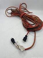 Full view of the coiled vintage power transfer cable showing its red and black coloring and attached paper tag.