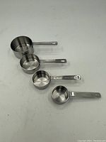 Four stainless steel measuring cups arranged side by side showing sizes and handles.