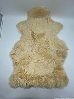 Top side view of natural cream sheepskin rug showing long curly wool fibers and irregular shape.