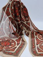 Silk scarf held up showing sheer fabric and multicolored abstract floral design in red, orange and beige tones.
