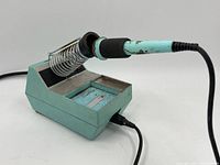 Green soldering iron station with soldering iron resting on coil holder and black power cord attached.