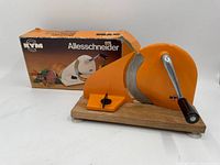 Vintage KYM Allesschneider slicer in orange color on wooden base with original box behind it.