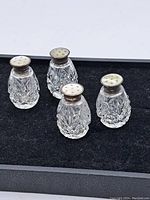 Four vintage crystal salt and pepper shakers with sterling silver caps arranged on black fabric.