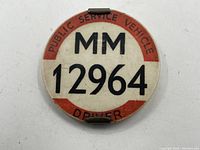 Front view of the vintage circular Public Service Vehicle Driver badge with ID MM 12964, showing text and condition.