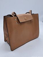 Front and side angled view of the rectangular tan textured purse showing overall shape and flap closure.