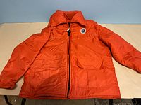 Front view of bright orange vintage jacket with zipper and two front pockets laid flat on surface.