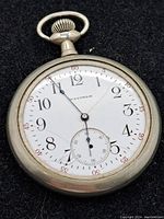 Front view of the Waltham pocket watch showing white dial with cracked glass and black Arabic numerals, minute markers in red, and small seconds subdial.