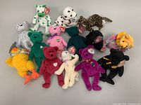 Fourteen assorted Ty Beanie Babies plush toys arranged together showing a variety of colors and animals including bears, dogs, duck, elephant, lamb and cat.