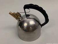 Front view of domed stainless steel kettle with scalloped black handle and brass whistle spout