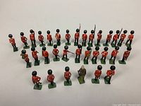 Photo displaying all 31 British lead Grenadier Guard figurines arranged in rows showing variety of poses and single khaki soldier.