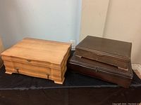 Three wooden flatware chests of different sizes and finishes shown on a black cloth surface