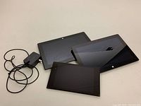 Three tablets and a power adapter laid out on table, angled view