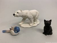 Three porcelain figurines: polar bear, bird, and cat on display against a white background.