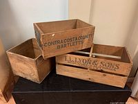 Three stacked vintage wooden crates on a black surface showing various stenciled labels and natural wood wear.