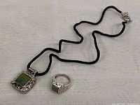 Photo of entire jewelry set showing the silver ring and pendant on black cord.