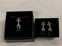 Full view of necklace with pendant and matching earrings on black display boxes showing green and clear cubic zirconia stones