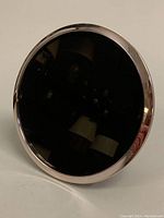 Side angled view showing circular mirror with shiny silver frame and dark backing.