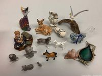View of assorted porcelain, ceramic, glass, and pewter figurines on white background showing various animals and people.