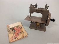 Children's Singer Sewhandy metal sewing machine next to the original instruction manual.