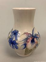 Frontal view of the Moorcroft bud vase showing pink and blue flowers with green leaves against a cream background.