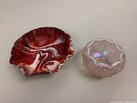 Top-angle photo showing the red/white marbleized milk glass bowl with bas-relief rose pattern next to the pink opalescent Fenton glass Lily of the Valley bowl.