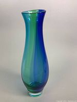 Front angle view of tall, slender blown glass vase in blue and green alternating vertical gradient with rounded base and flared top rim.