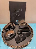 Photo of five assorted black belts of different styles and sizes arranged on a tray with leopard print edge.