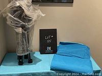 Folded teal beach blanket next to a wrapped black metal chair frame on a teal mat.