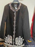 Front full view of black women's car coat with white decorative embroidery on hem and white trim along front button closure and neckline.
