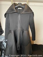 Front view of black long sleeve coat/dress with large collar, front zipper, and textured panels on sleeves and pockets.