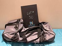 Side view of grey and black duffle bag with wheels and a handle, lying flat on a surface.