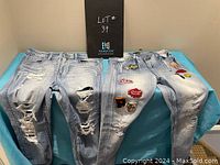 Two pairs of women's funky jeans displayed on a table, showing heavy distressing on one pair and colorful patches on the other.