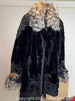 Back view of mid-length black fur coat with two-toned fur trim on hood, cuffs, shoulders, and hem.