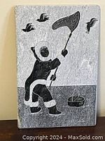 Front view of rectangular Inuit stone carving showing a figure in traditional clothing holding a bird net capturing birds flying above, with a basket at the figure's feet.