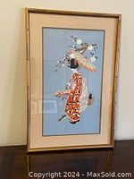 Full view of the embroidered Geisha picture with gold-colored frame showing overall appearance and size relative to surroundings.