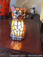 Front view of the stained glass kitten lamp illuminated on a wooden surface showing the colors and design.