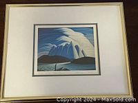 Framed print by Lawren Harris titled "Lake and Mountains" showing stylized blue and white mountains, lake, and clouds, with a thin gold-colored frame and white matting.
