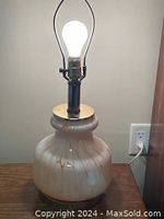 Glass table lamp with beige and brown swirl pattern on a white background. Lamp is 22 inches tall with a bulbous base and metal fittings at the top including the socket and harp holder. Light bulb installed, no lampshade included.