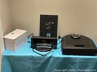 Neato robot vacuum, charging dock, and box of replacement filters on a blue cloth surface against a plain wall.