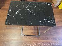 Top-down view of black faux marble tabletop and chrome base on wooden floor.