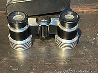 Close-up of Remington 3X coated opera glasses on a black surface showing clear lenses and some wear on metal body.