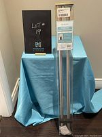 Photo of the sealed Teagan dual shower rod in original packaging standing upright on a blue draped surface.