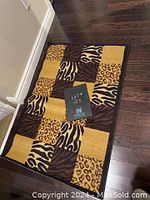 Rectangular area rug with zebra and leopard print blocks in shades of yellow, brown and black on a dark hardwood floor.
