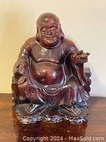 Front view of the wooden smiling Buddha statue showing facial features, rounded belly, detailed robes, and base.