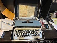 Smith Corona typewriter with keyboard visible, original case, manual inside case, placed on a desk with papers and mouse nearby.
