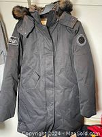 Front view of grey winter jacket with hood and fur collar, showing zip and snap buttons, and sleeves with Toboggan logo patches.