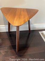 Front view of triangular teak table with three legs on dark wood floor